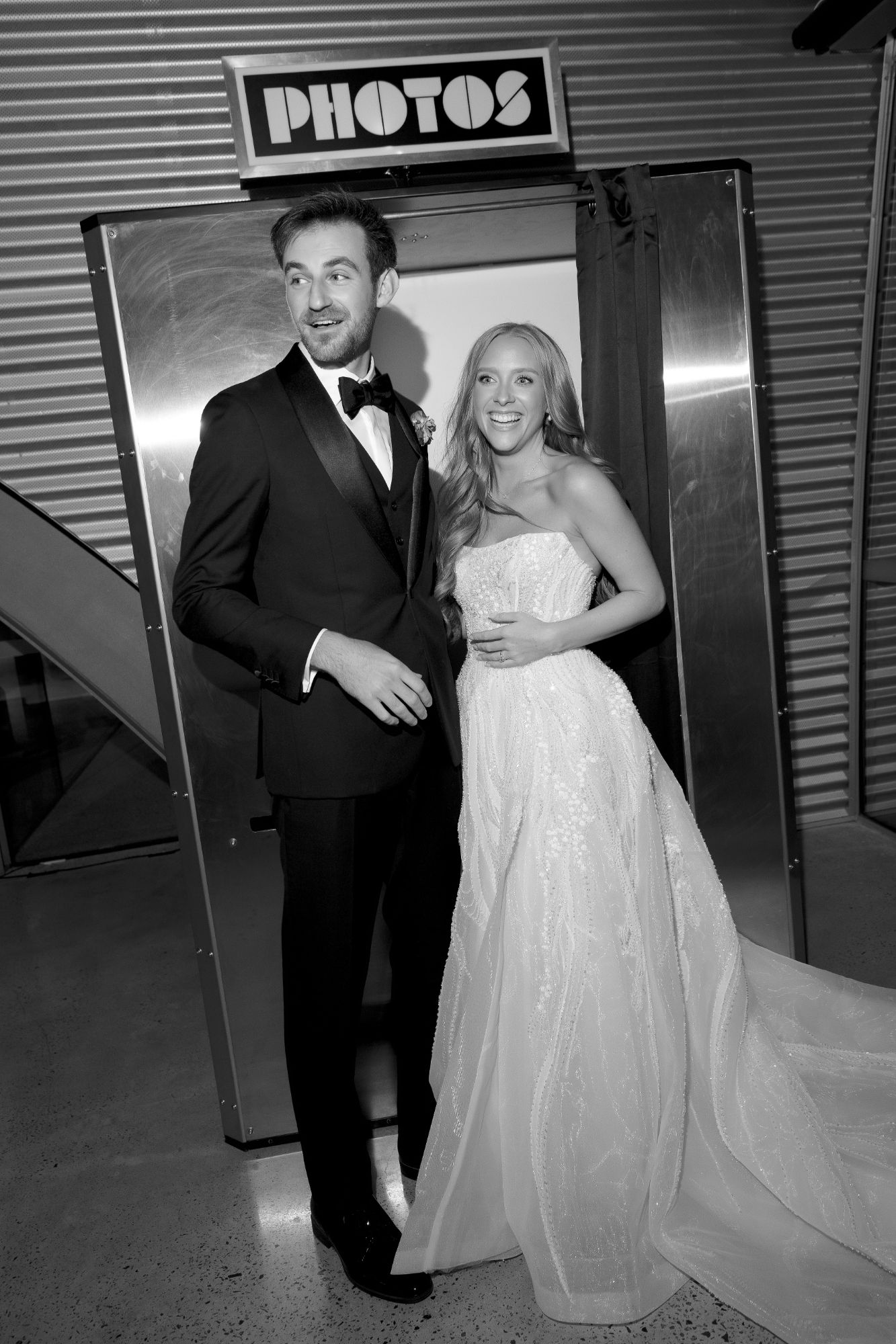Bride and groom laughing in front of a stainless steel Retro Booth with a PHOTOS sign